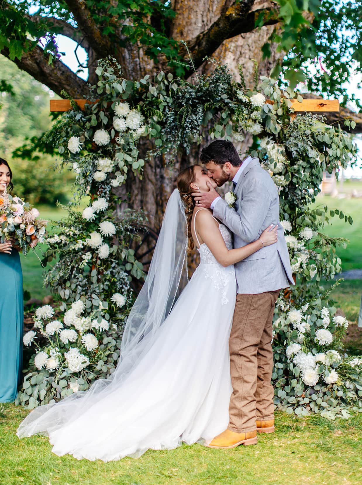 bride and groom share first kiss in front of floral arch during wedding ceremony at knotting hill farm in jordanville ny