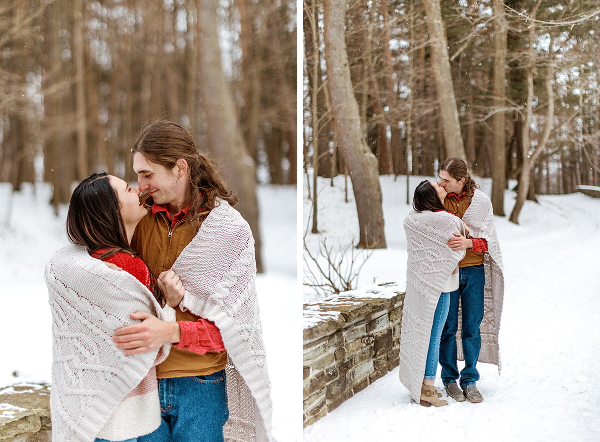 Couple stands on a stone bridge and snuggles under a blanket during winter engagement photos in Upstate NY