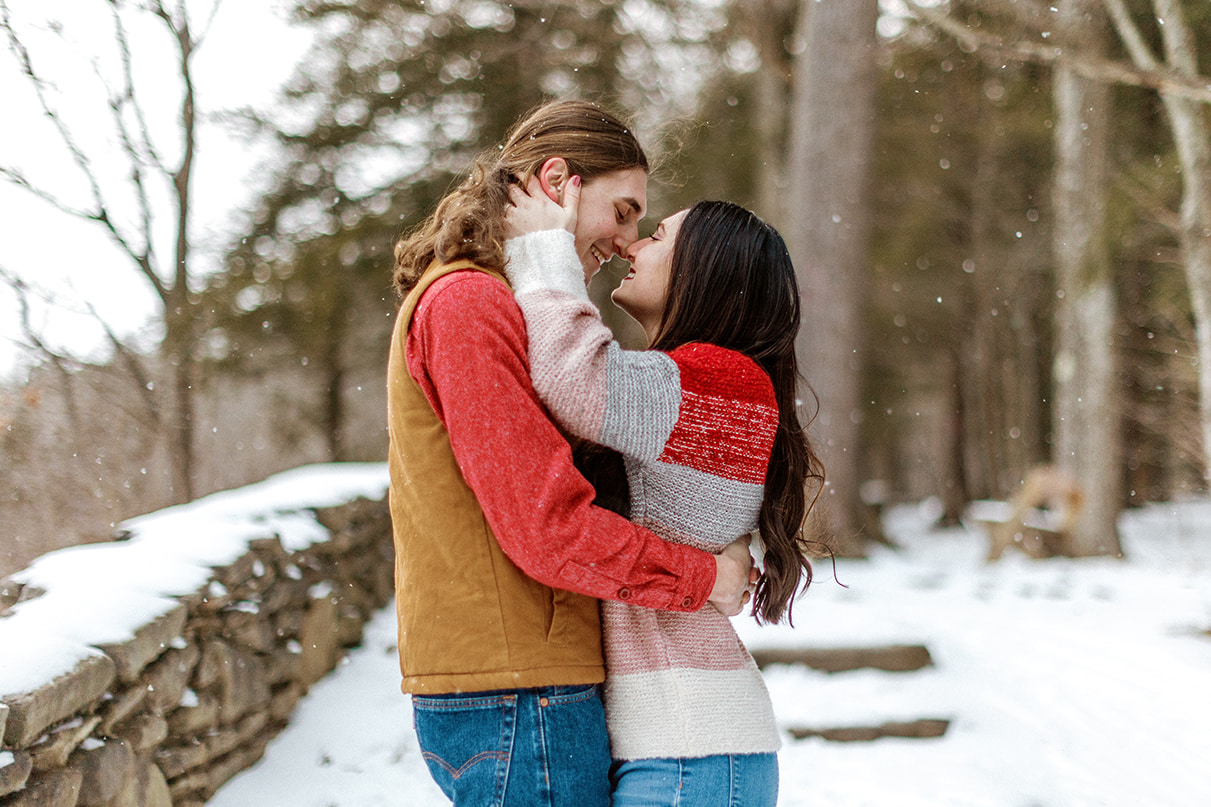 Couple smiles and almost kisses during snowy winter engagement session at Letchworth State Park in Upstate NY