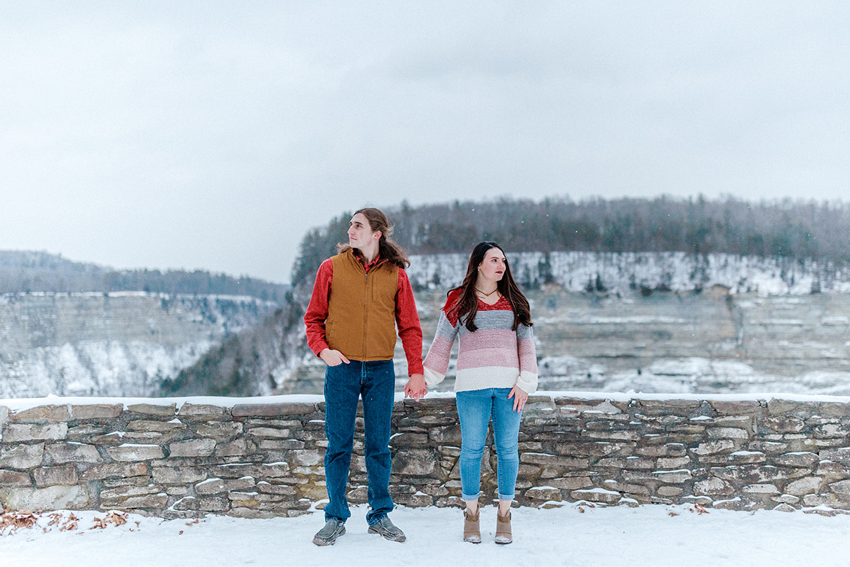 Couple holds hands and looks in opposite direction while standing near entrance to Letchworth State Park in Castile, NY