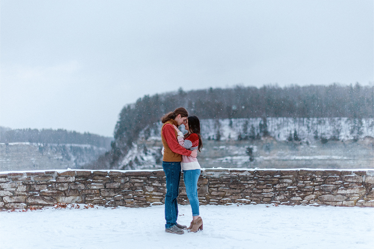 Snow falls while couple stands and embraces in front of gorge in Letchworth State Park in Upstate NY