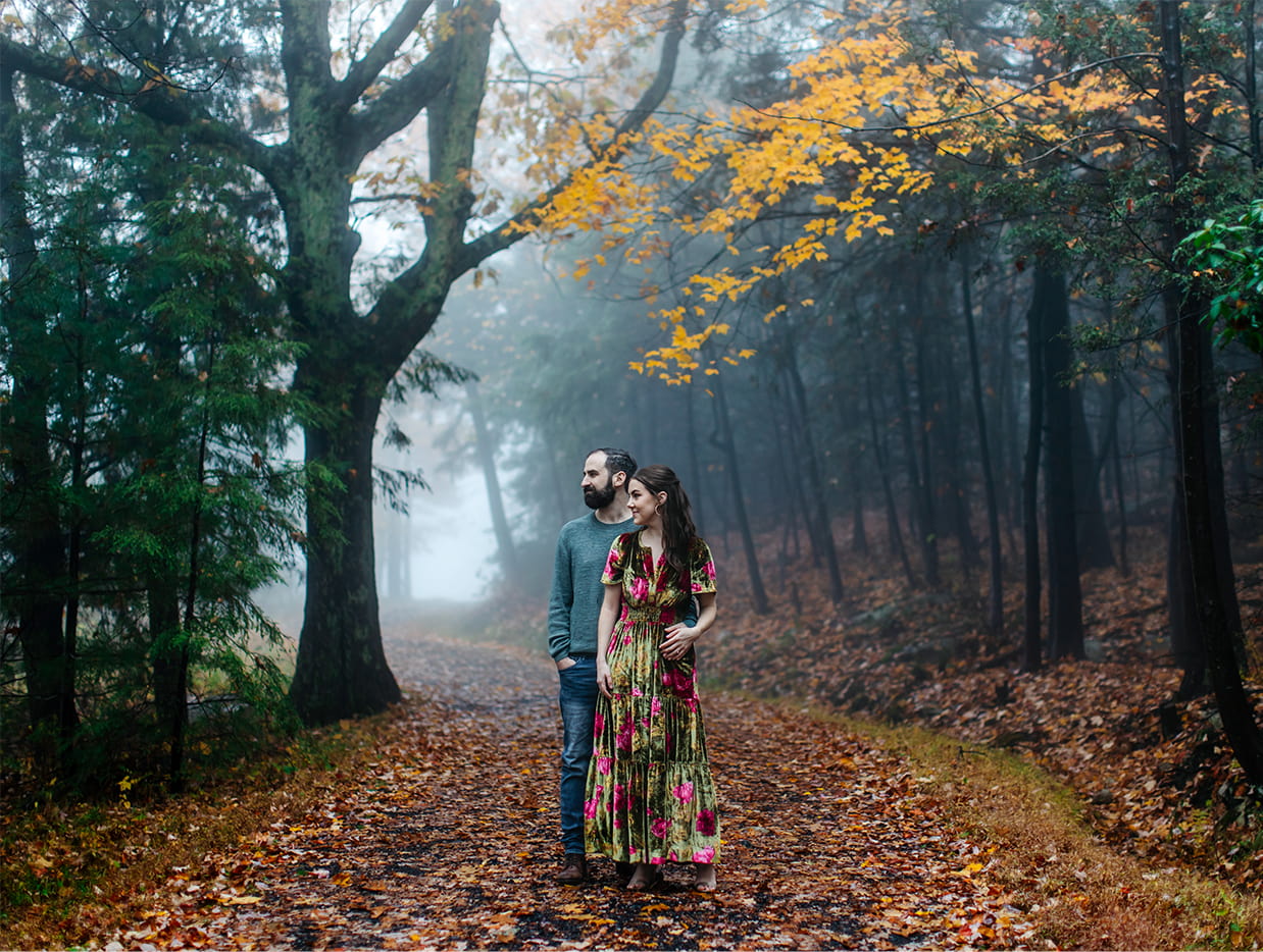 couple stands on foggy pathway covered in leaves during engagement session at Minnewaska State Park in Kerhonkson, NY