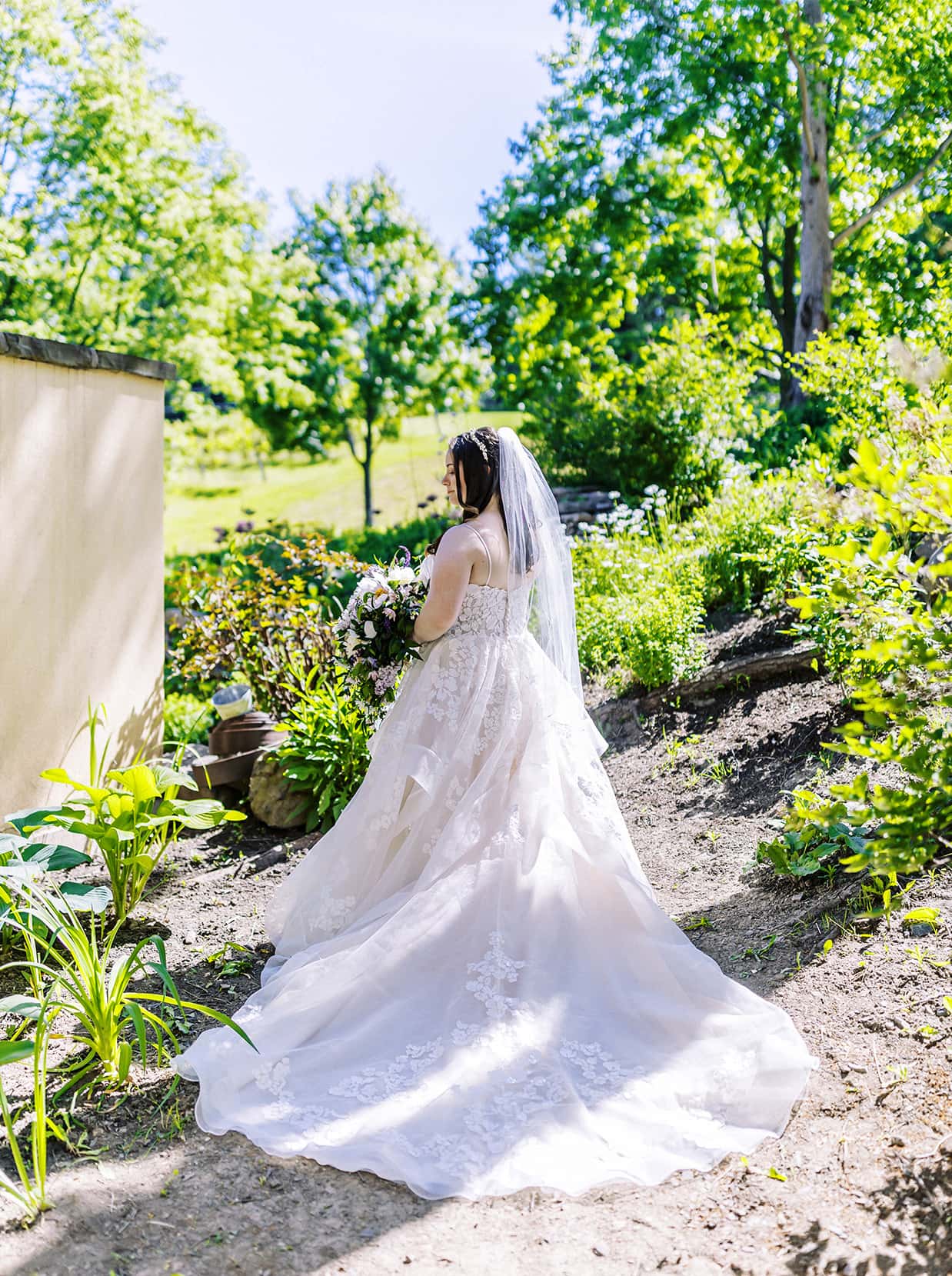 Bride shows off the back of her wedding dress in garden at mirbeau inn and spa Skaneateles