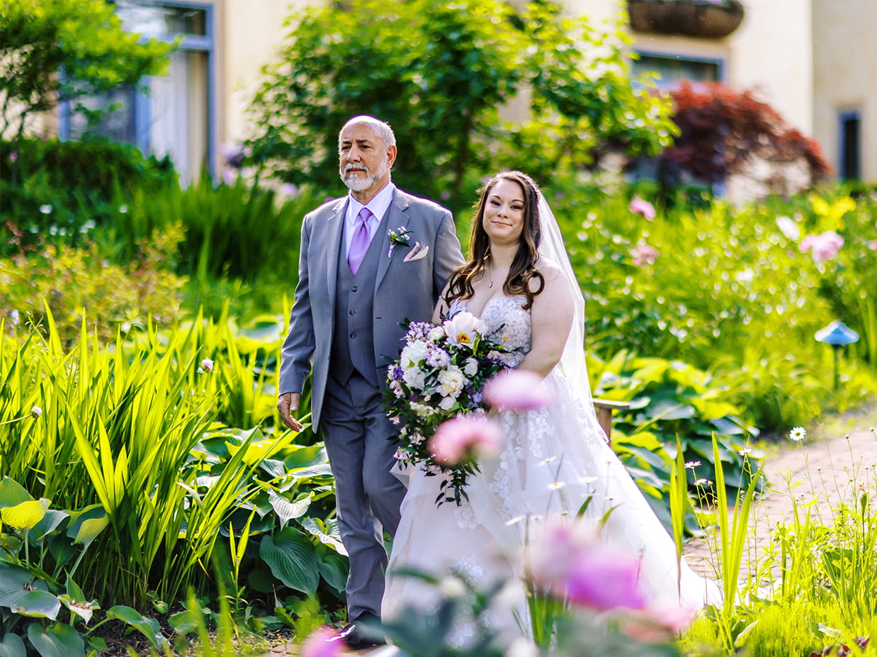 bride's father walks her through lush garden path to ceremony at mirbeau