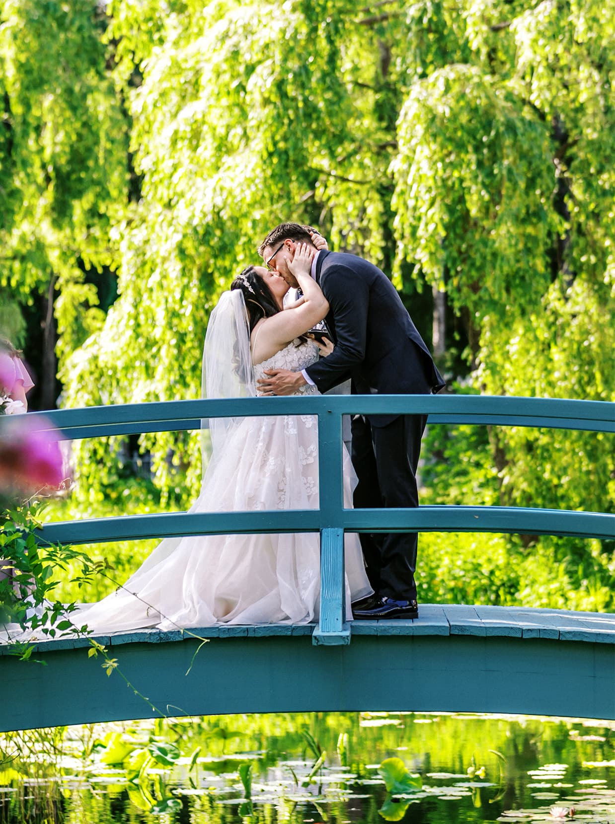 bride and groom share first kiss on blue bridge over koi pond