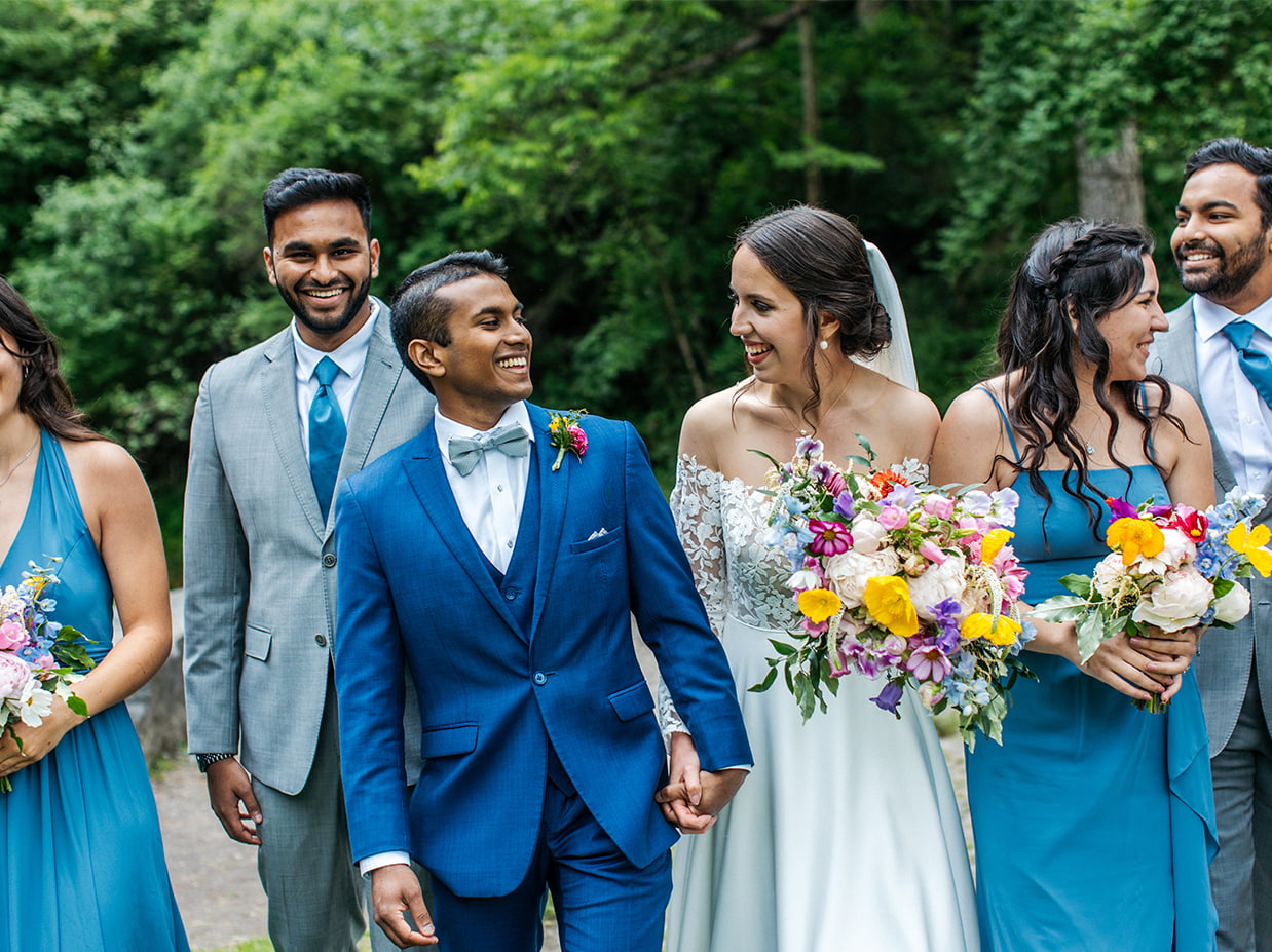 bride and groom laugh as they walk together with their wedding party towards the camera
