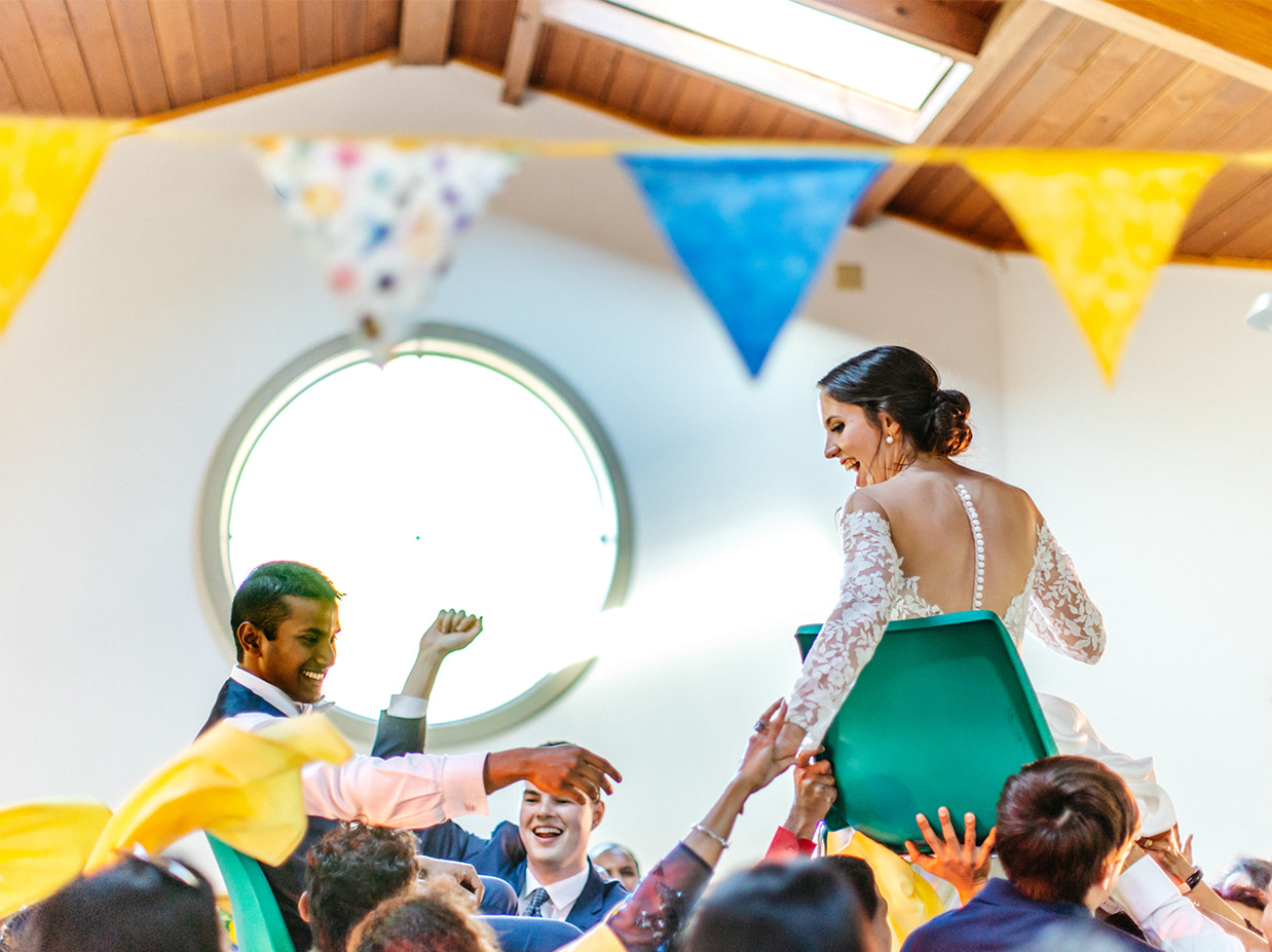 bride and groom are lifted up on chairs during colorful blue and yellow wedding reception