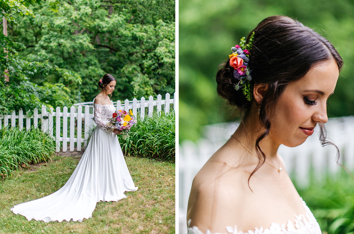 bride stands in front of white picket fence holding colorful bouquet with bright colored flowers in her hair