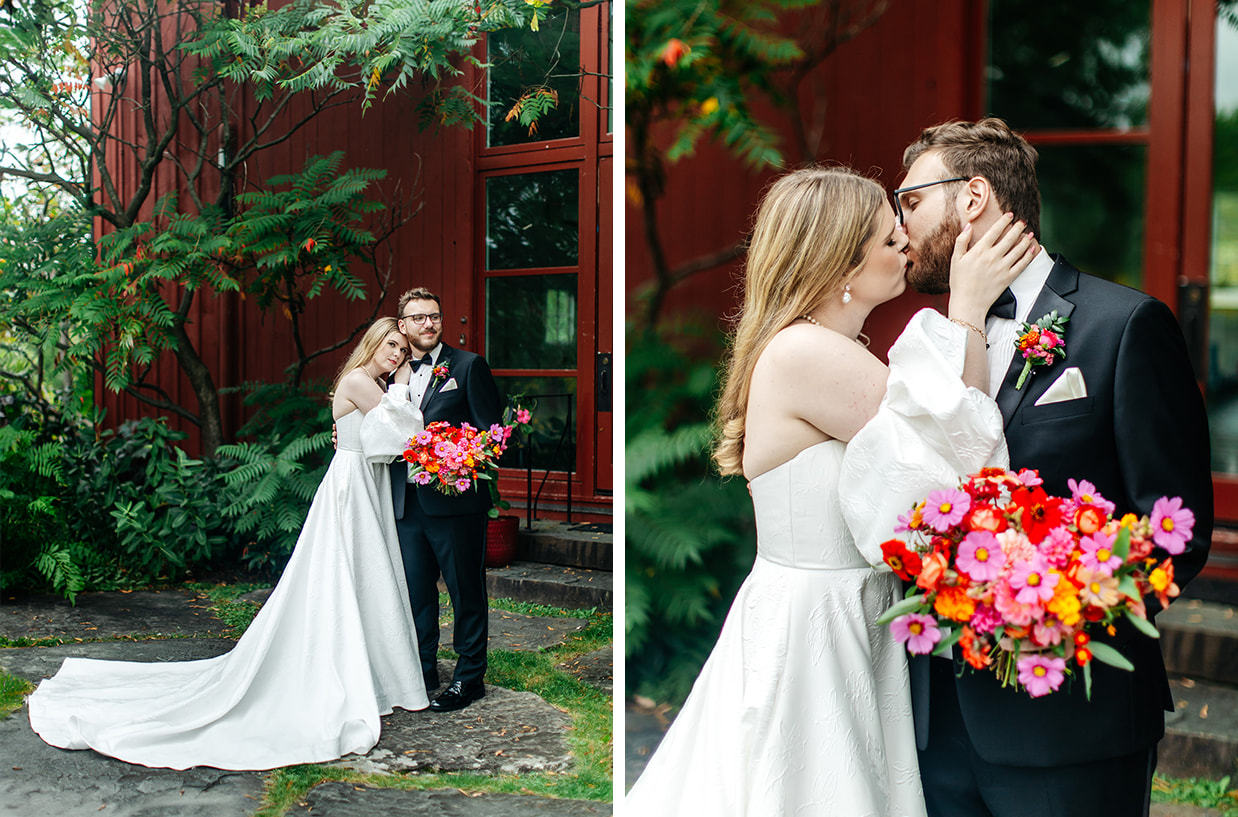 bride and groom stand together holding a colorful bouquet in front of the red painted barn of the treman center in newfield NY
