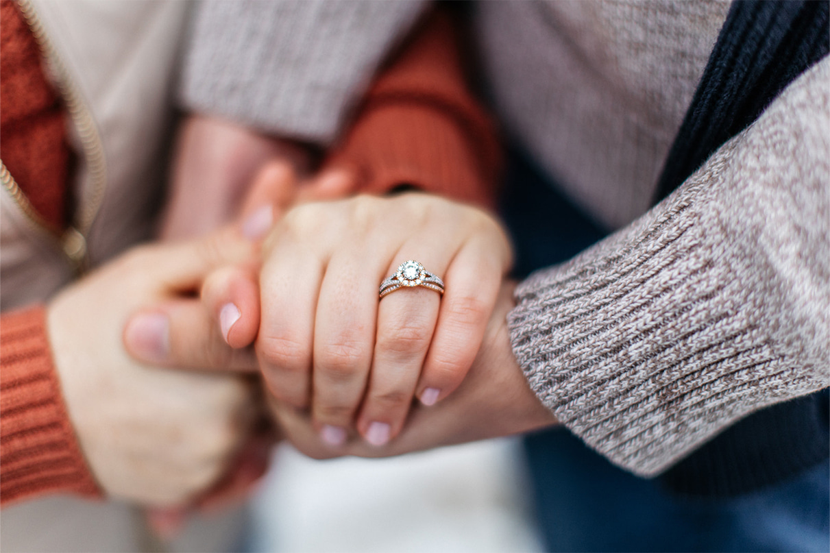 man and woman hold hands. woman has a mixed metal white and yellow gold diamond halo engagement ring on her finger