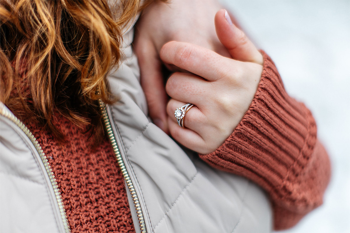 woman holds mans hand while wearing a mixed metal yellow and gold diamond halo engagement ring on her finger