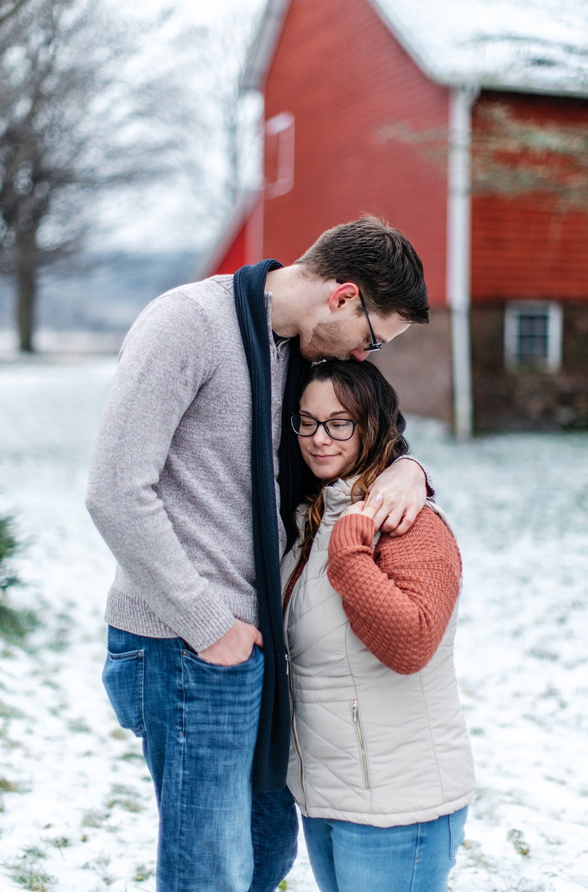 man kisses the top of womans forehead during the engagement session on a christmas tree farm in upstate ny