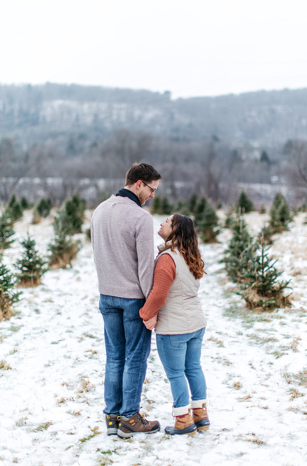man and woman stand on snowy pathway holding hands and looking at each other during their winter engagement session in upstate ny