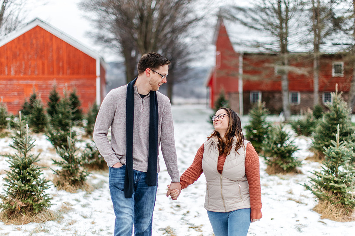 couple walks together smiling and holding hands during engagement session at a christmas tree farm in upstate ny